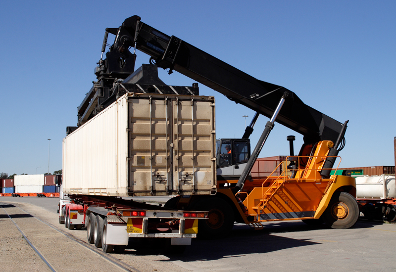 Reach stacker loading a shipping container onto a truck chassis at a container yard